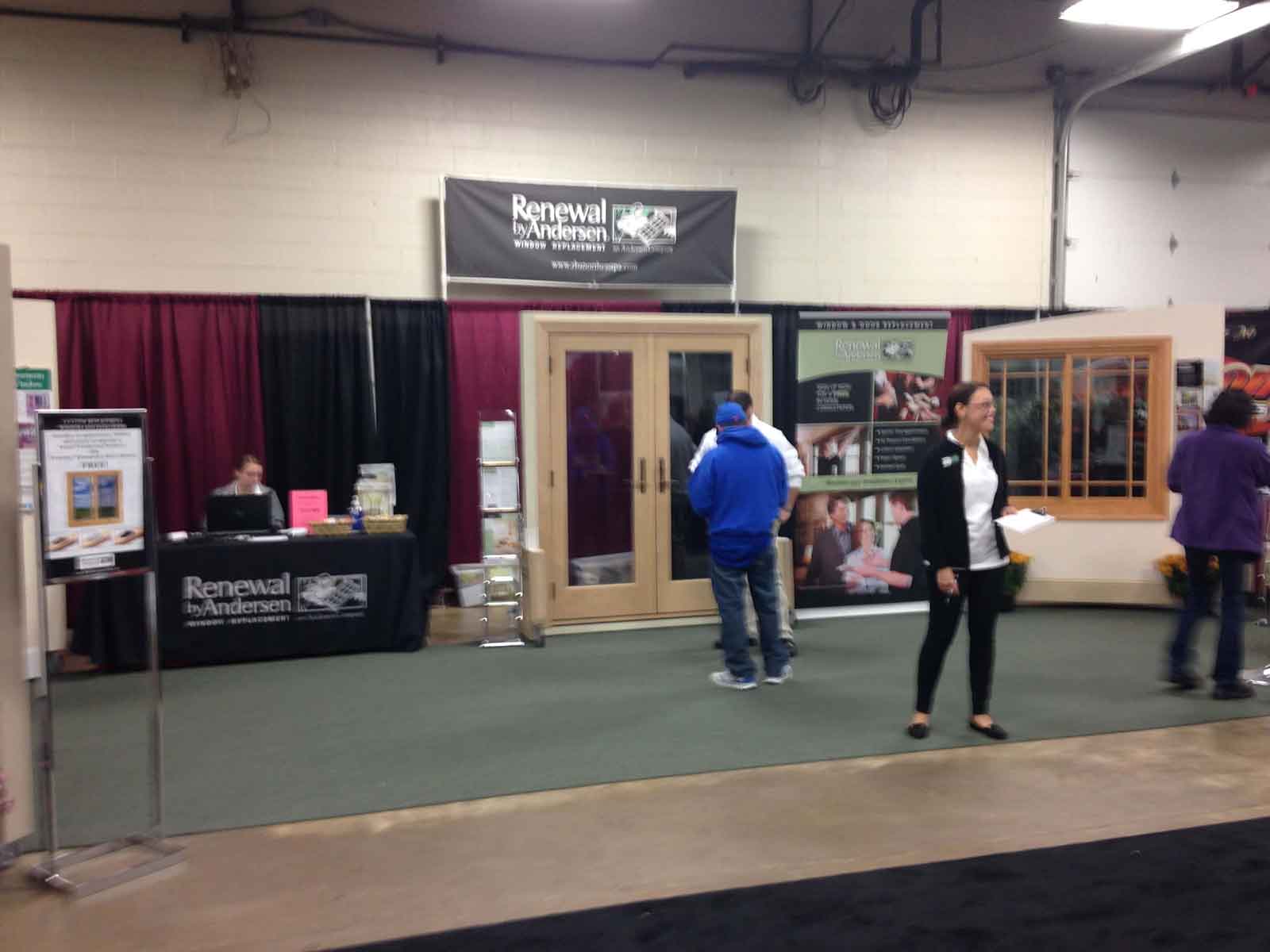 Samantha waits to greet guests at the Home Show, while Richard goes over the features and benefits of RbA's patio doors with a customer.